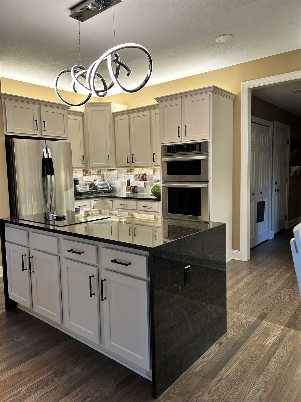 Kitchen remodel with island, white cabinets, and sculptural lighting by Stellar Construction